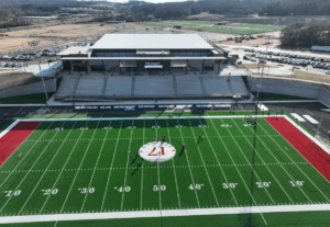 A wide view of a football field with stands and a building in the background.