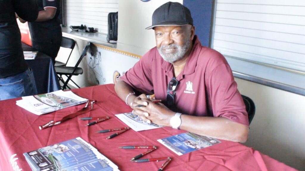 Smiling man in a cap sits at a table with various tools.