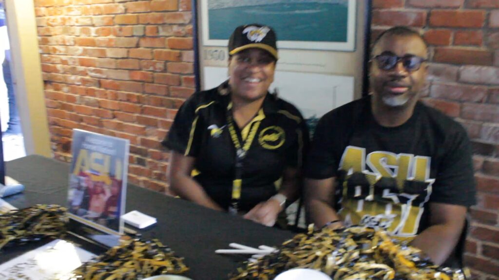 Two people in black and gold sports attire at a booth.