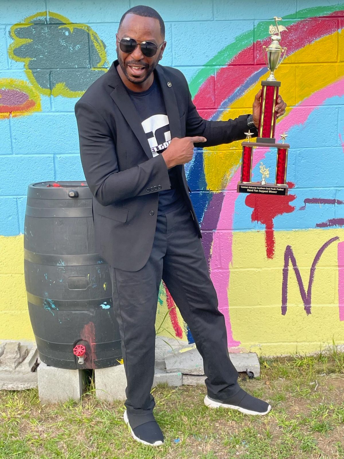 Man in black holding a bottle and a red device outdoors.