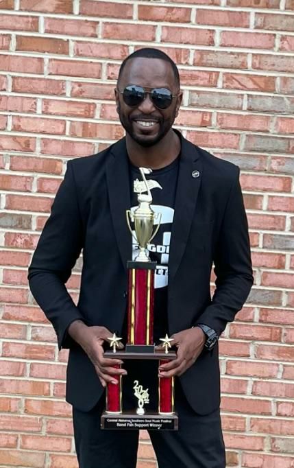 Man in black jacket holding a tall trophy with a smiling face.
