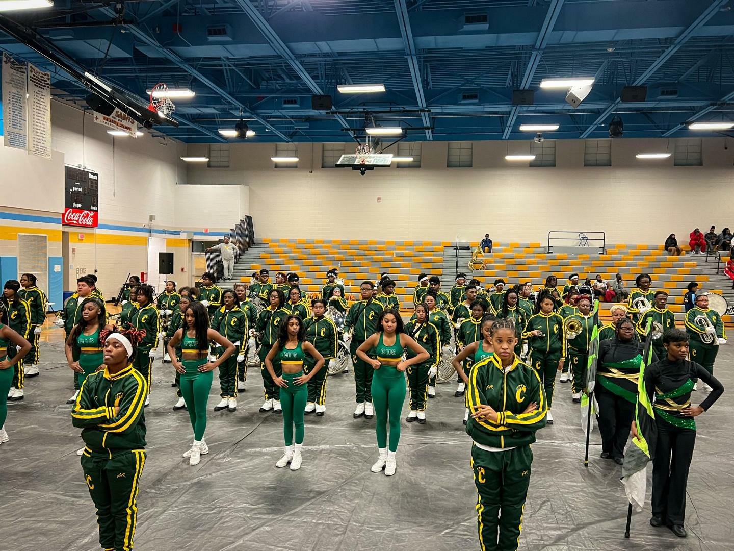 A large group of cheerleaders in green and yellow uniforms performing indoors.