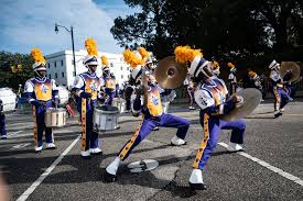 Cheerleaders in purple and gold uniforms perform with pom-poms and a megaphone during a lively parade.