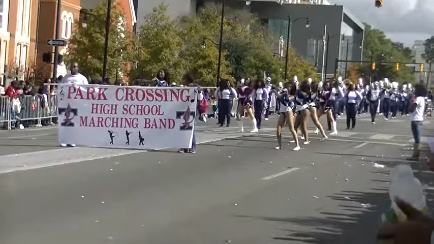 High school marching band and cheerleaders parade down a street.