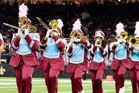 Marching band playing brass instruments in uniform on field.