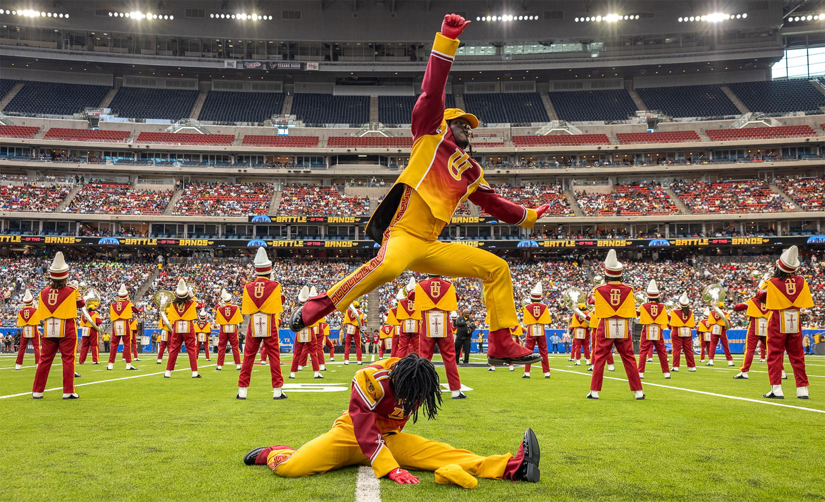 Marching band members perform an energetic dance routine in a stadium.
