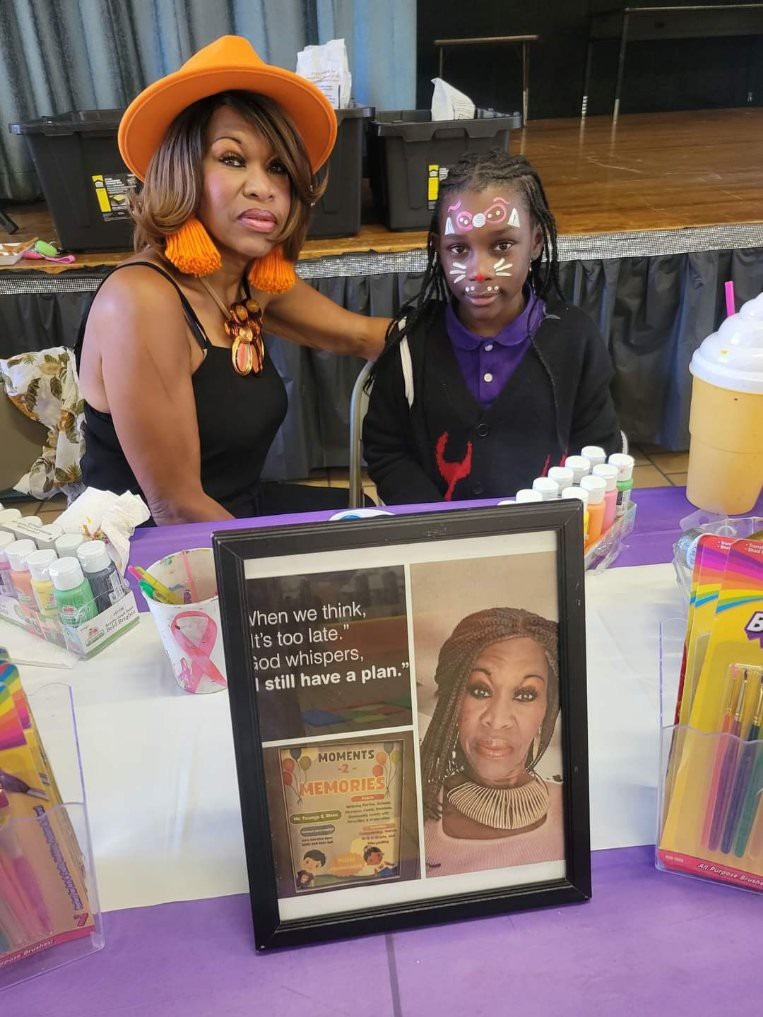Two women at a table with framed photos and crafts.