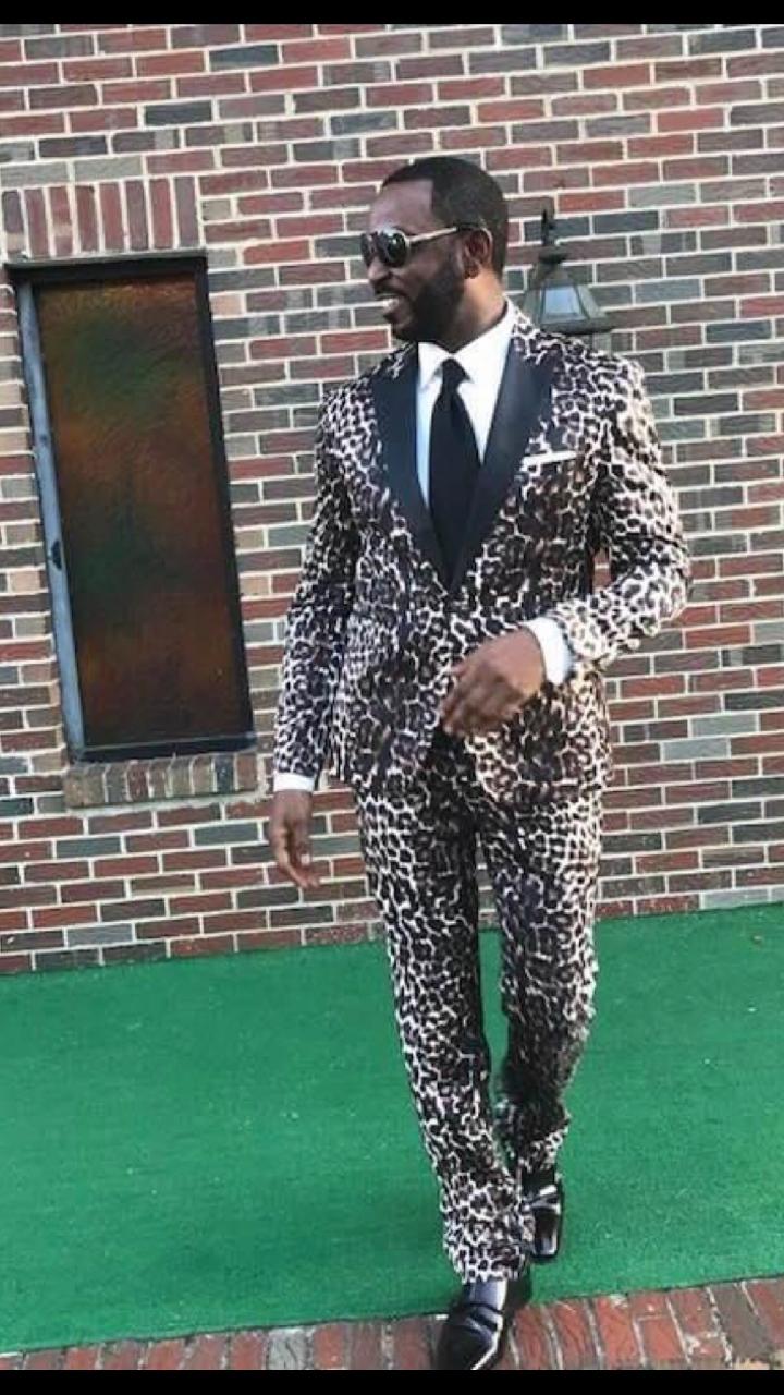 Man in a bold leopard print suit posing outdoors.
