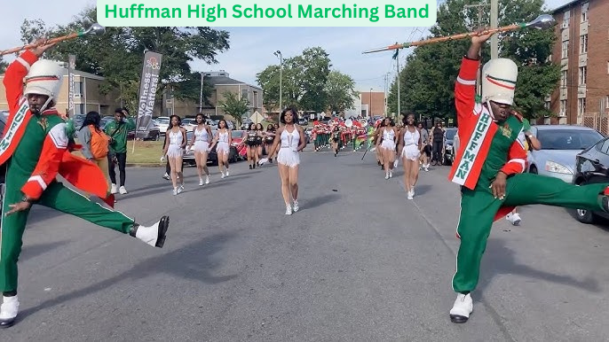 Marching band parades down the street in uniform with a mascot leading.