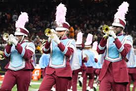 Marching band in maroon and light blue uniforms playing trumpets.